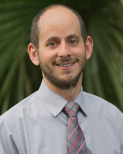A man in a dress shirt and tie smiling for the camera.